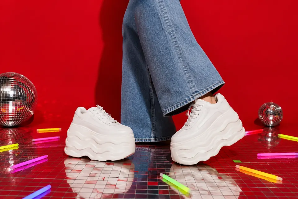 Ein Paar weiße Turnschuhe mit extrem dicker, welliger Plateausohle zwischen verstreuten Knicklichtern