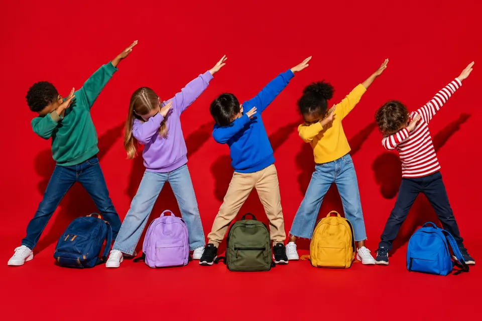 Mehrere Kinder machen auf dem Schulhof gleichzeitig die Dab-Pose mit dem Gesicht in der Armbeuge und schräg ausgestrecktem Arm