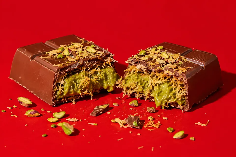 Eine dicke, in der Mitte durchgebrochene Schokoladentafel mit grüner Pistaziencreme und knusprigen goldenen Teigfäden