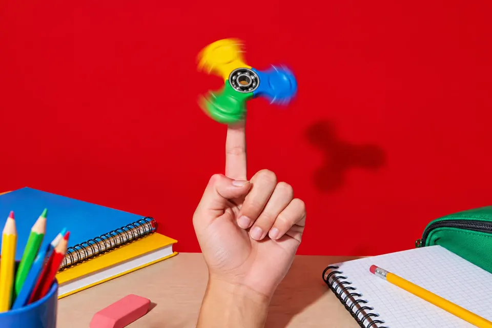 Bunter Fidget Spinner mit drei Armen dreht sich auf einer Fingerspitze über einem Schultisch