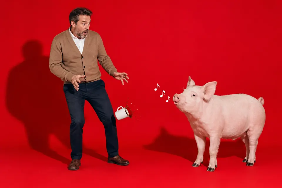Fassungsloser Mann lässt seine Tasse fallen, neben ihm steht ein pfeifendes Schwein