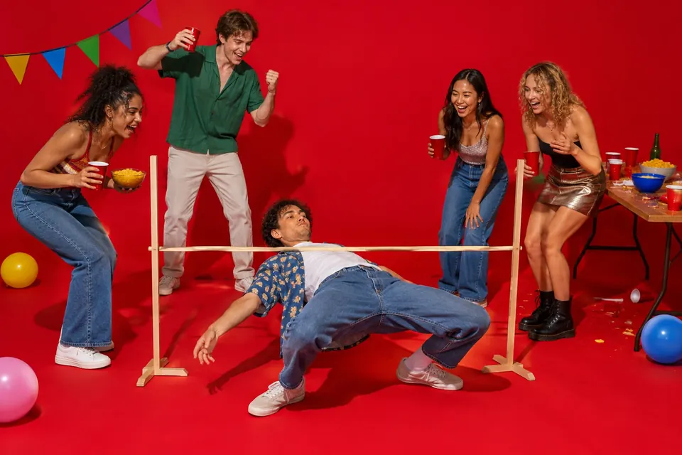 Freunde feiern eine Party, eine Person tanzt Limbo unter einer fast bodennahen Stange