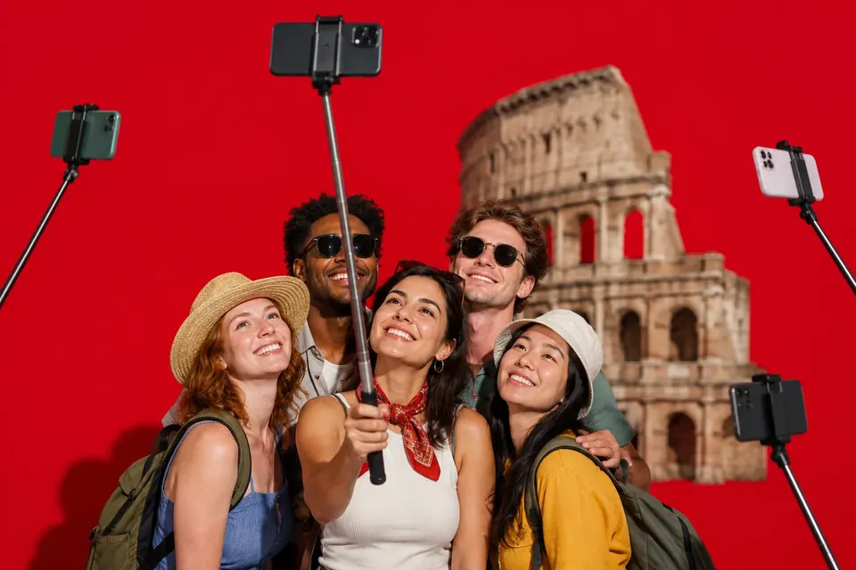 Eine Gruppe Touristen lächelt in ein Smartphone, das an einer langen ausziehbaren Stange über ihnen hängt