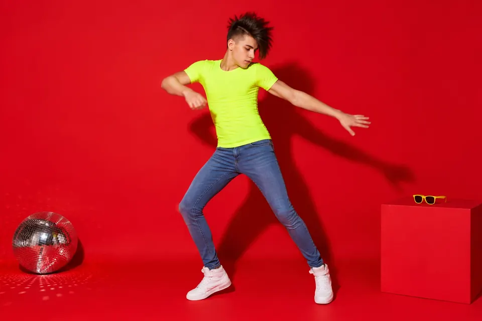 Jugendlicher mit stacheliger Frisur, Neon-Shirt und Röhrenjeans tanzt mit schnellen Armbewegungen im Club