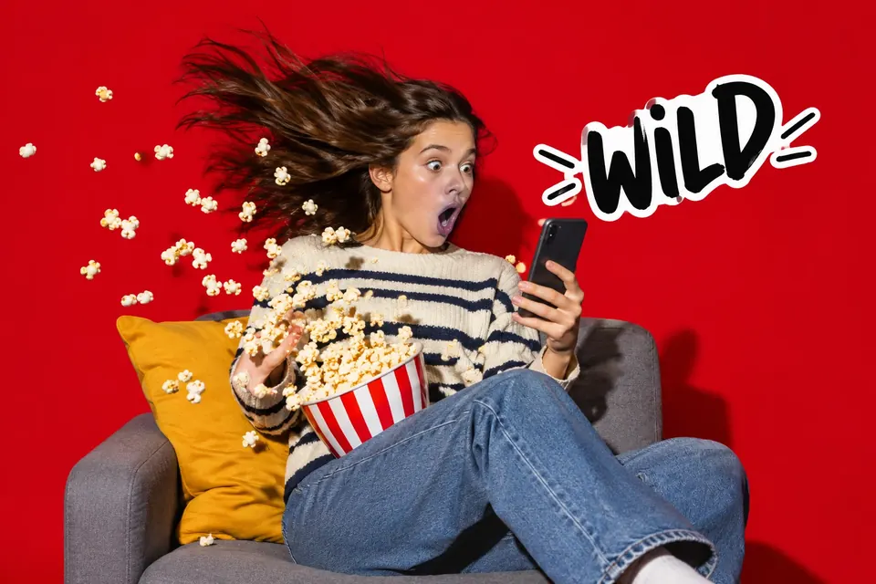 Jugendlicher starrt mit offenem Mund aufs Handy, Popcorn fliegt durch die Luft
